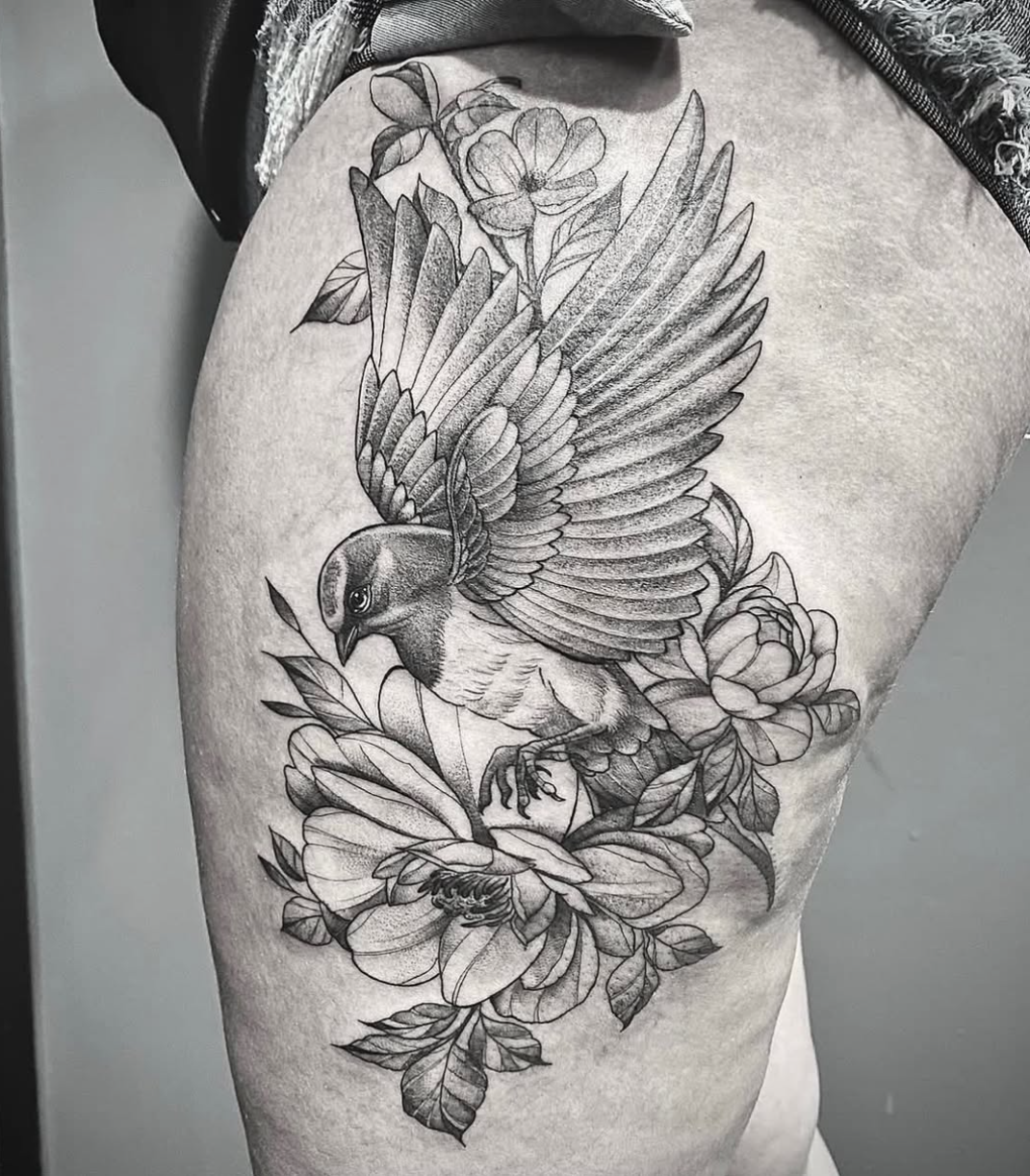 Tatuagem de pássaro com flores na coxa em preto e cinza, trabalho de Ricardo Marinho
